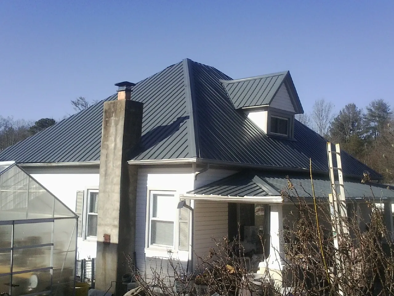 Dark blue standing seam metal roof on a white farmhouse with dormer — Slate & Tile Roof Repair by Roofing Brothers in Eighty Four