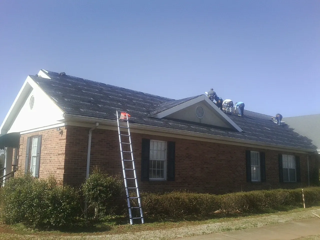 Crew tearing shingles off a brick ranch roof with a ladder set — Metal Roof Repair work by our crew in Eighty Four