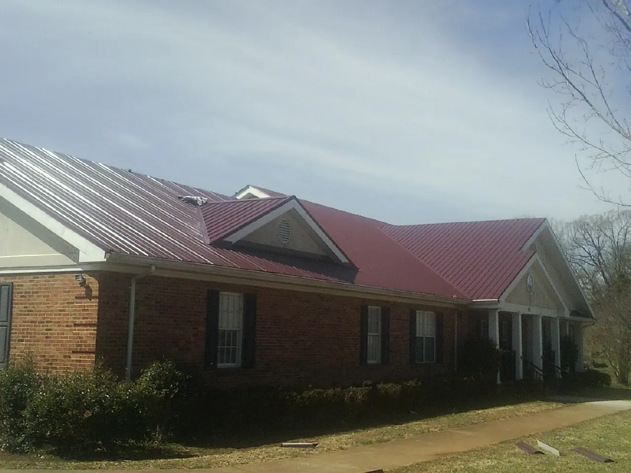 Red metal roof with gabled entries on a long brick building, from a Hail Damage Roof Repair job in Eighty Four