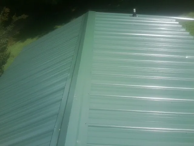 New green metal panels meeting at the ridge of a roof — Flat Roof Repair work by our crew in Eighty Four