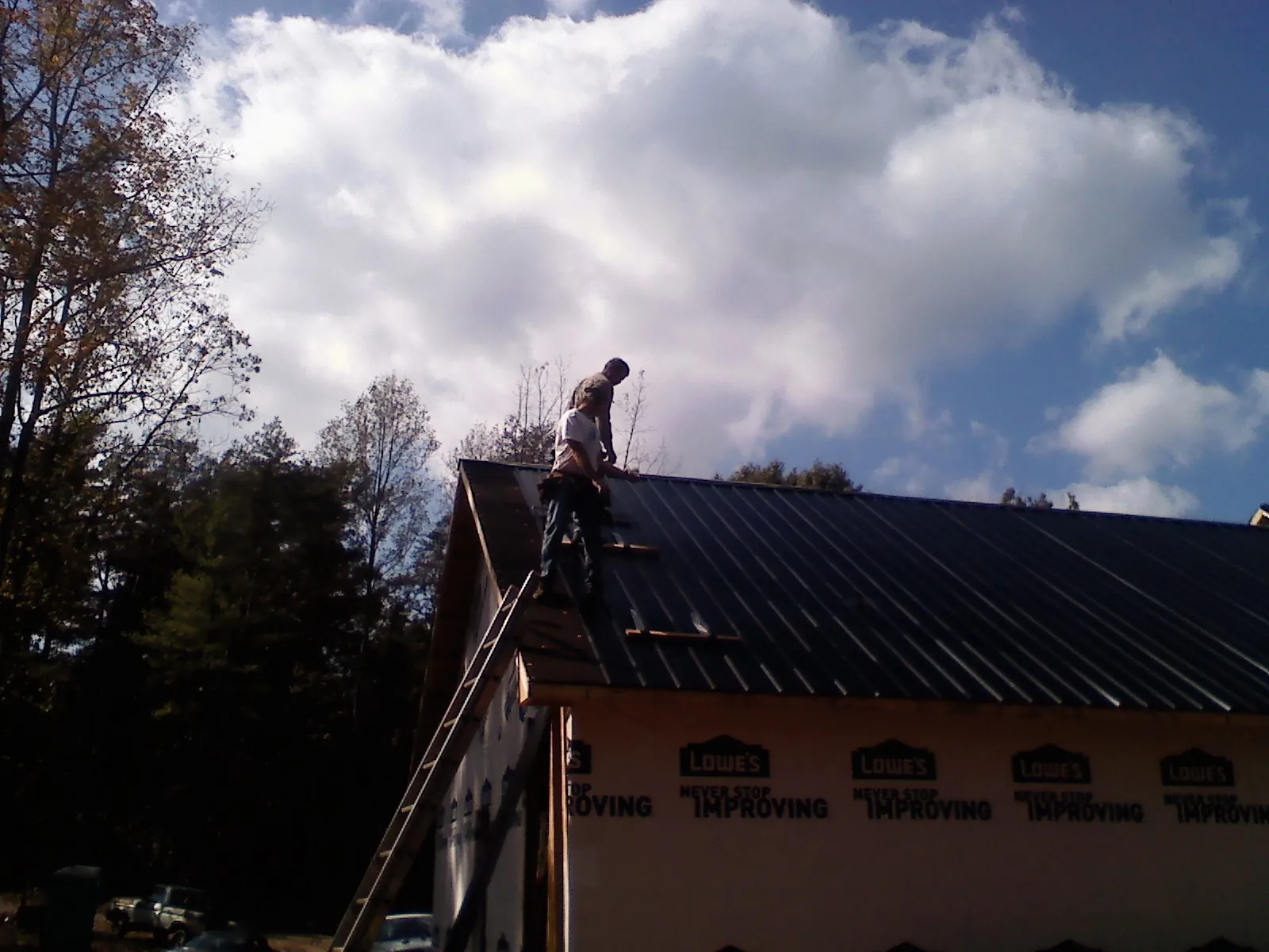Roofer fastening dark metal panels high against a cloudy sky, from a Roof Inspection job in Eighty Four