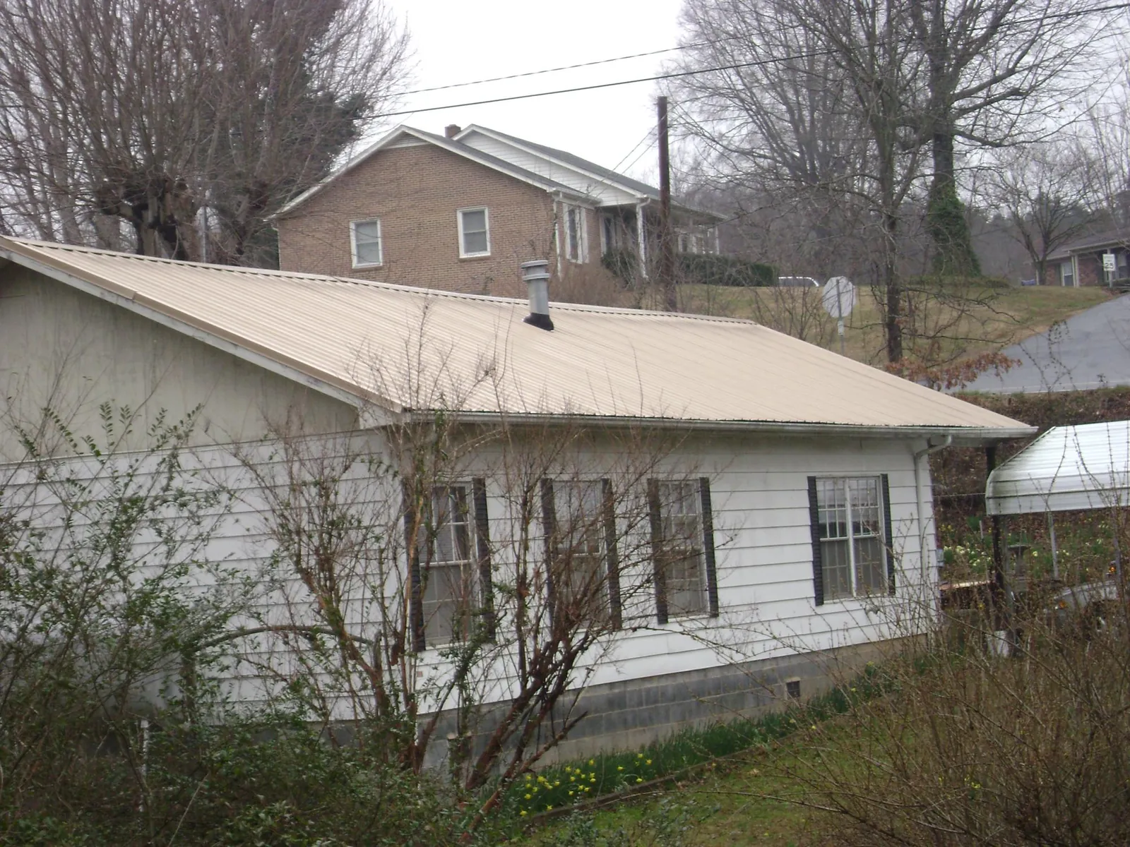 Tan metal roof on a white sided house set into a hillside — Commercial Roofing by Roofing Brothers in Eighty Four